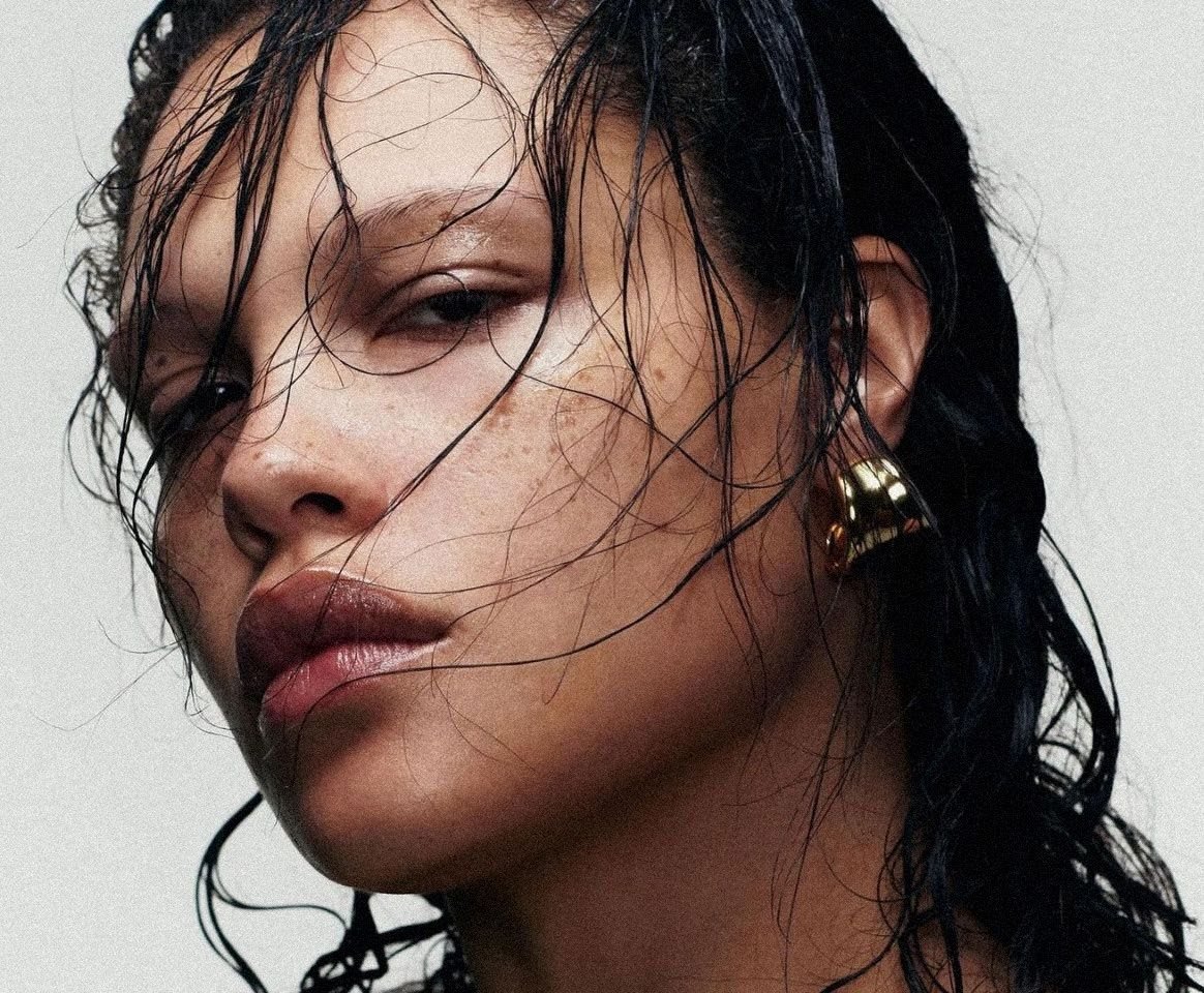 Primer plano del rostro de una mujer con el cabello mojado sobre la cara y un arete dorado.